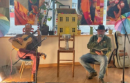 two men on a stage playing instruments and reading from a book